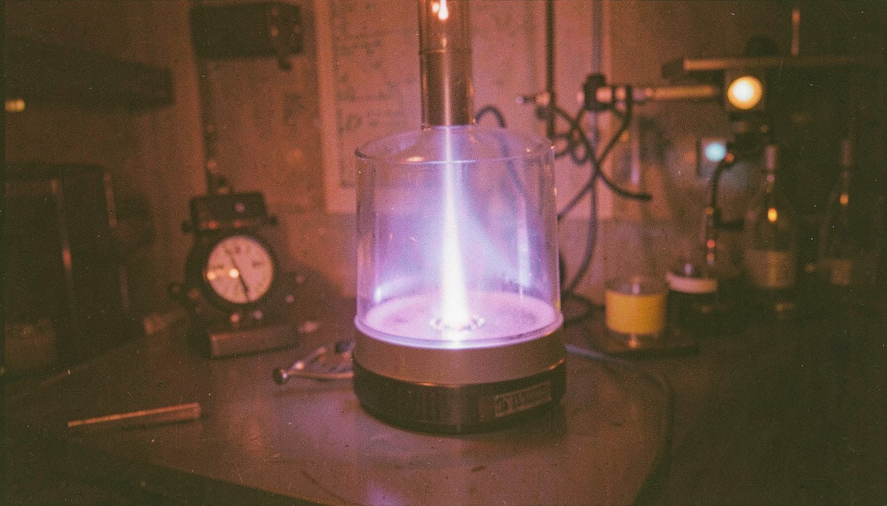 Analog film photograph of a laboratory plasma discharge chamber glowing violet and pale blue in a darkened laboratory, fine grain, quiet scientific mood