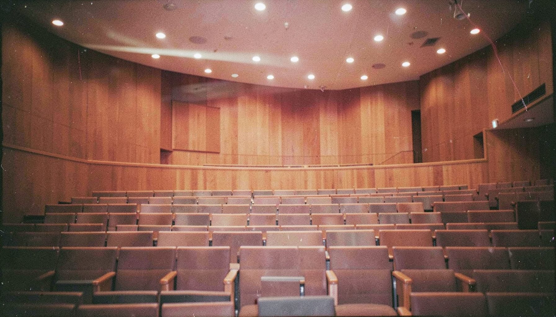 Analog film photograph of a modern conference auditorium with tiered seating, warm wood paneling and soft overhead lighting
