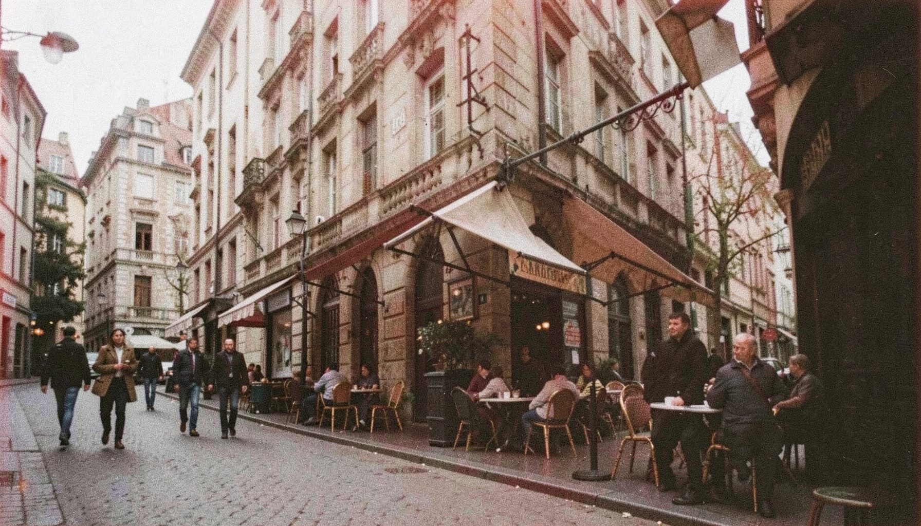 Analog photograph of a historic northern European city street with stone architecture, café terraces and pedestrians in soft daylight